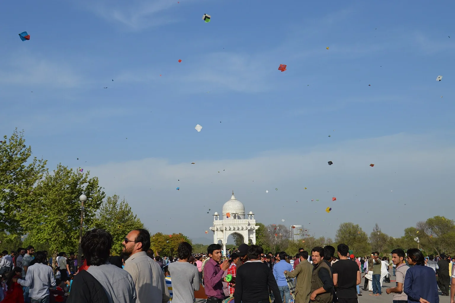 A Basant crowd in Pakistan under a sky scattered with colourful kites
