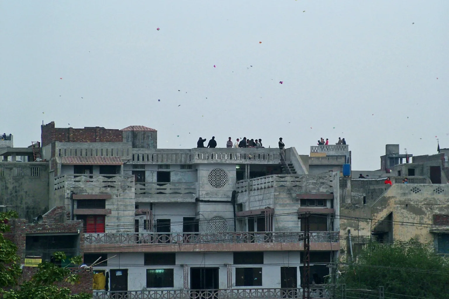 Old Lahore rooftops with people on them and kites in the sky above