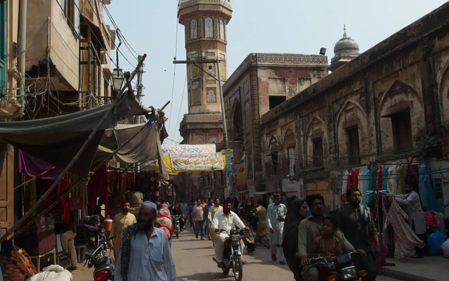 A walled-city bazaar street in Lahore beneath a mosque minaret